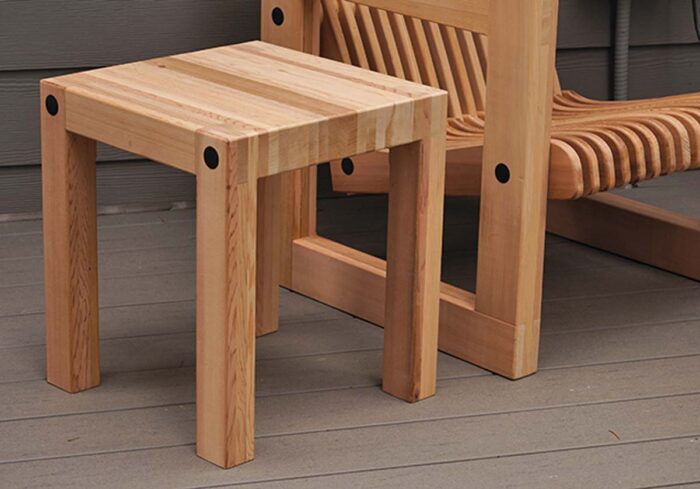 Abitcher block style side table made of cedar. Has exposed black hardware where the leg joins the top.
