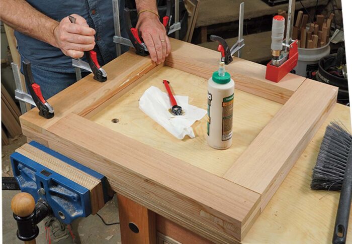 Asa clamps a final board in place. Glue squeeze out is visible, and there are several clamps holding the board in place. 