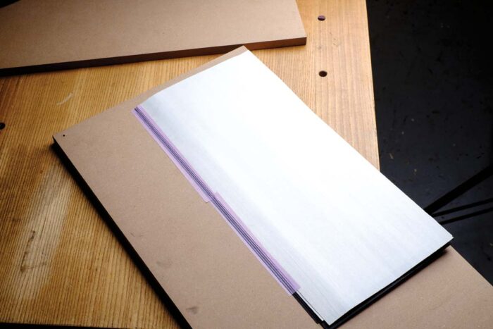 Several layers of black and white veneer are secured to a piece of MDF with purple tape.
